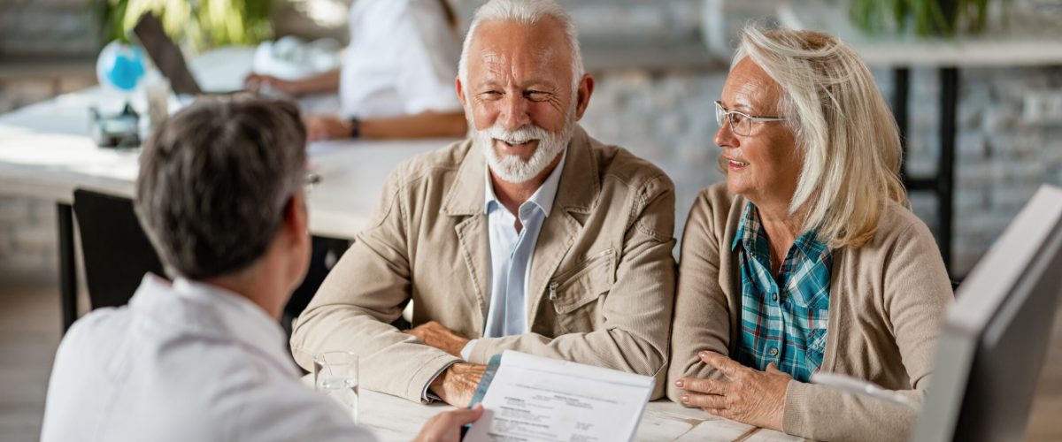 Happy senior couple communicating with a doctor about their health insurance while going through paperwork.